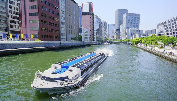 River cruise boat on Osaka canal with city skyline, part of Osaka Amazing Pass experience.