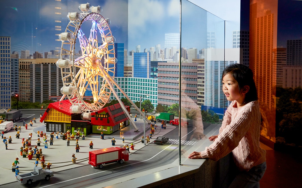 Child observing LEGO cityscape with Ferris wheel at LEGOLAND Discovery Centre.
