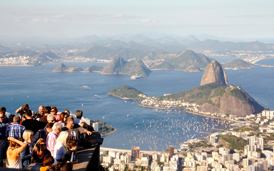 Crowd enjoying panoramic view of Rio de Janeiro from Christ the Redeemer viewpoint, with Sugarloaf Mountain.