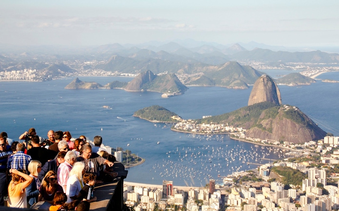 Crowd enjoying panoramic view of Rio de Janeiro from Christ the Redeemer viewpoint, with Sugarloaf Mountain.