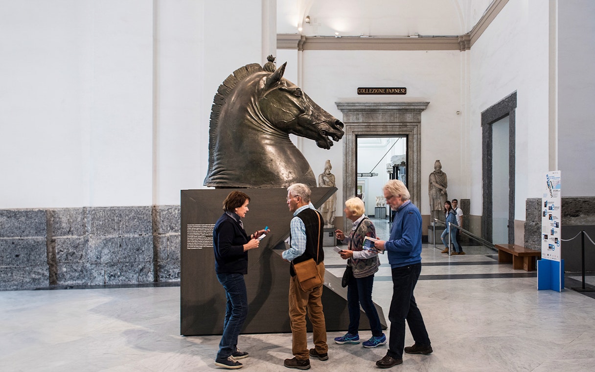 Visitors examining a horse sculpture at Naples National Archaeological Museum.
