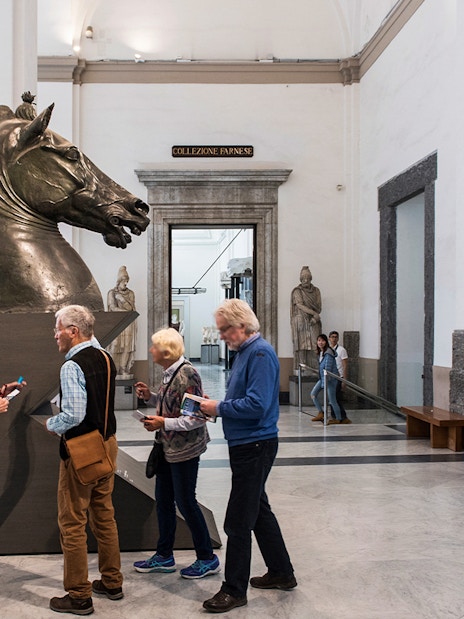 Visitors examining a horse sculpture at Naples National Archaeological Museum.
