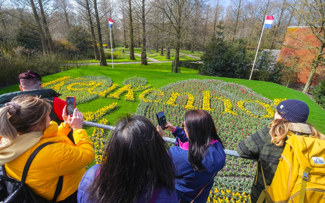 Visitors photographing tulip display spelling "Keukenhof" in Keukenhof Gardens, Netherlands.