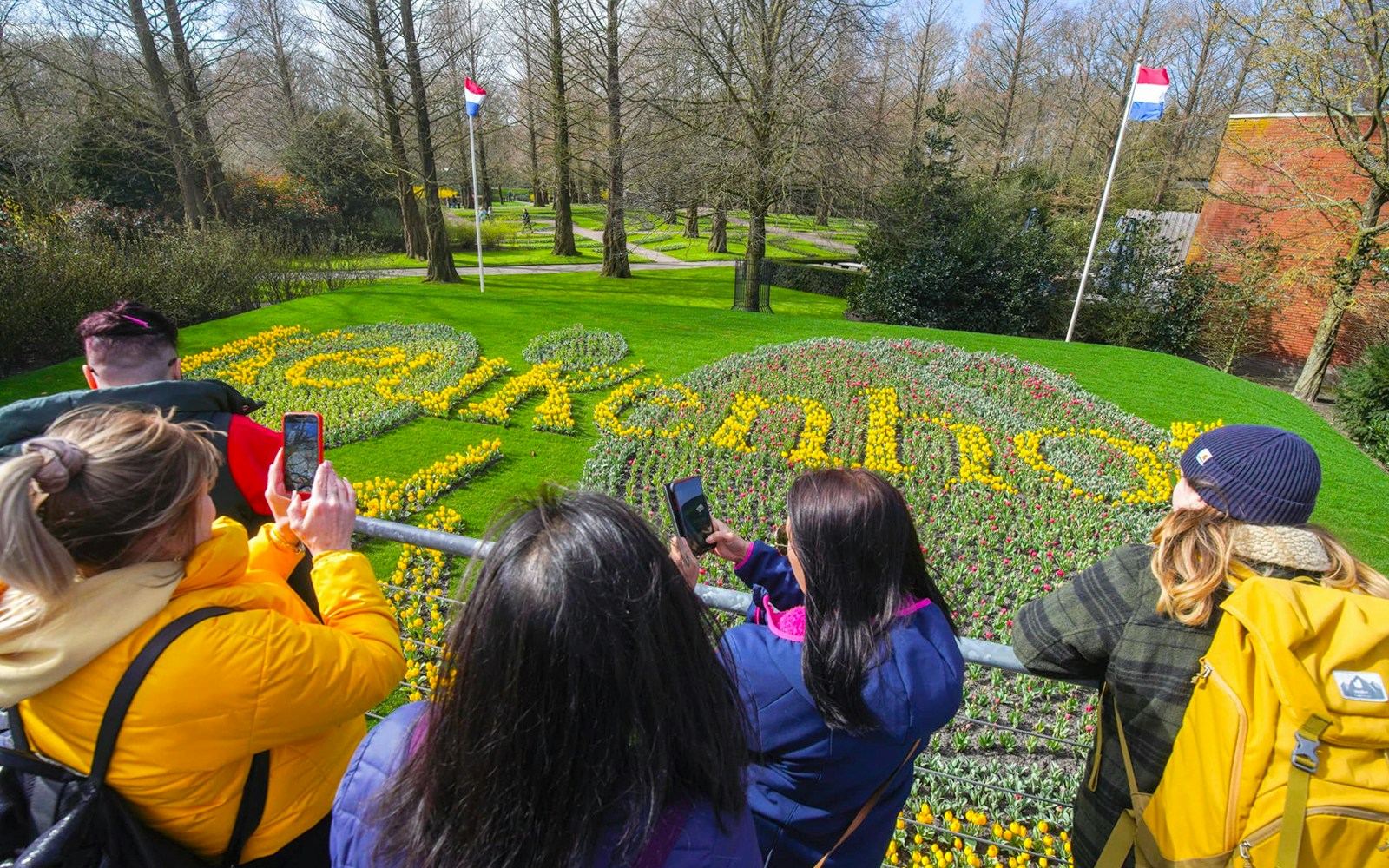 Visitors photographing tulip display spelling "Keukenhof" in Keukenhof Gardens, Netherlands.