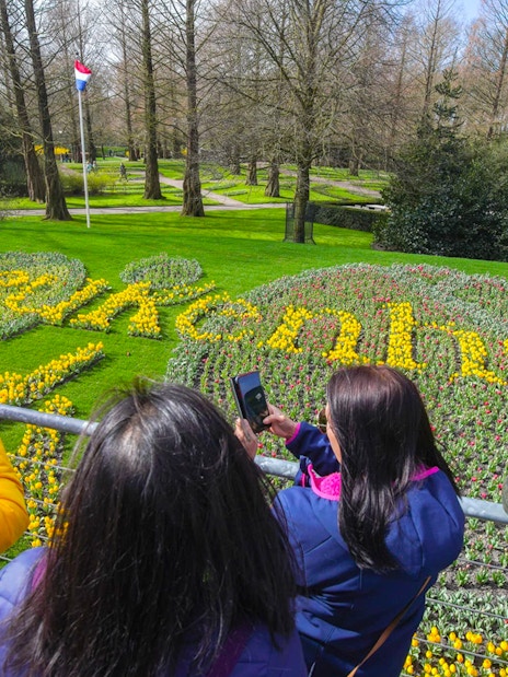 Visitors photographing tulip display spelling "Keukenhof" in Keukenhof Gardens, Netherlands.