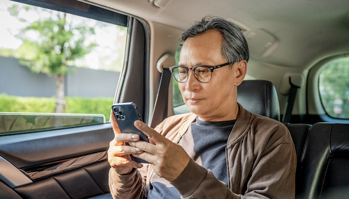 Man using smartphone in private car transfer from Singapore Changi Airport.