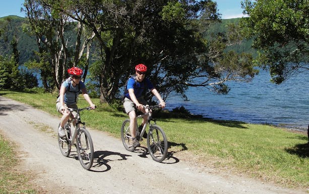 Bikers on a trail by a lake during a guided tour at Furnas.