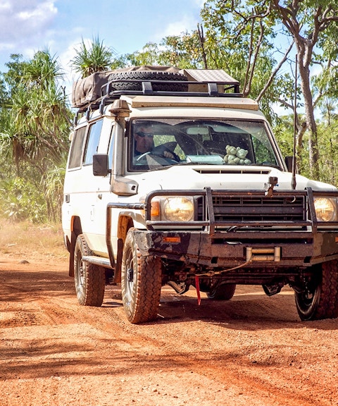 4WD vehicle driving on a dirt road through a forest on Moreton Island.