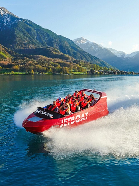 Jetboat speeding across Lake Brienz with passengers, surrounded by mountains.