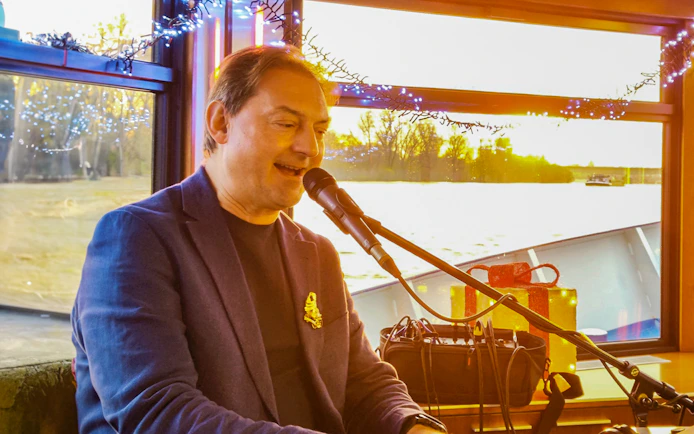 Musician performing on a boat during Cologne Advent tour with festive decorations.