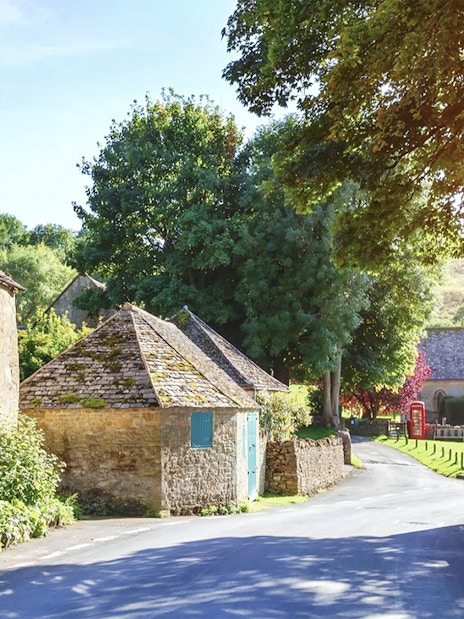 Cotswolds village street with stone cottages and lush greenery, part of small group tour.