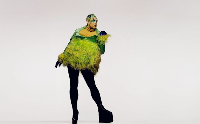 Person in a green feathered outfit with black leggings and platform shoes, Fergus Greer session.