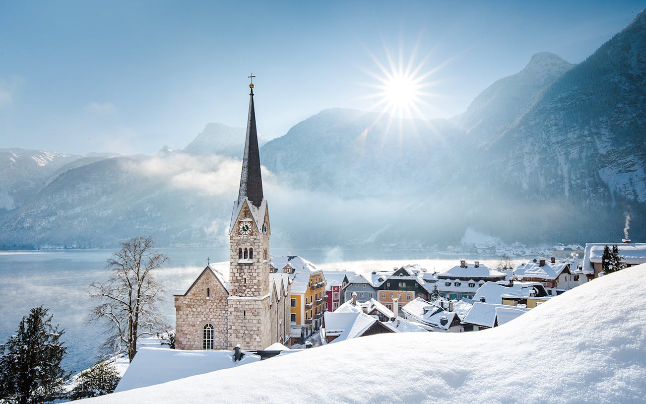 Church and snow-covered village in Hallstatt, Austria, with mountains in winter.