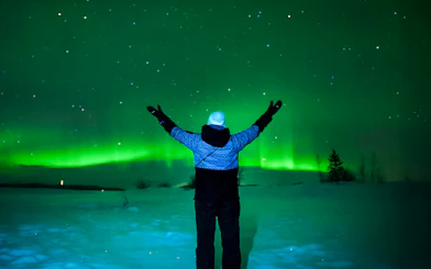 Person viewing Northern Lights in Tromso, Norway, with arms raised.
