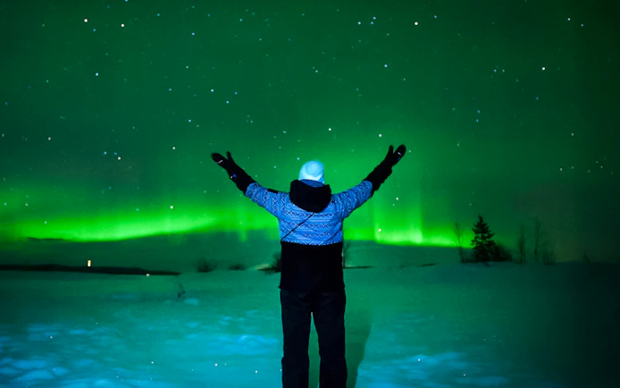 Person viewing Northern Lights in Tromso, Norway, with arms raised.