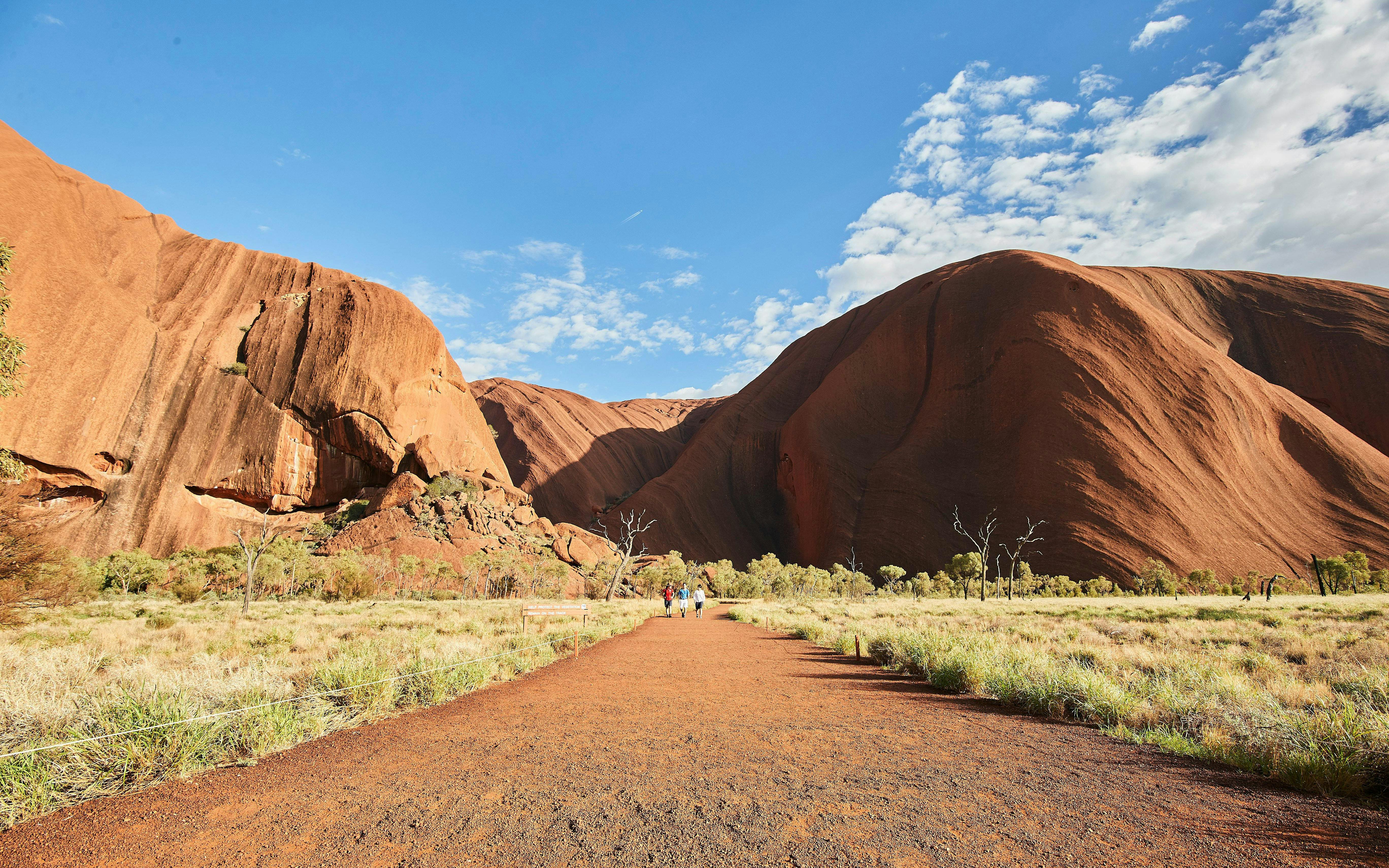 Uluru at sunrise with tourists walking on a guided tour, Australia.
