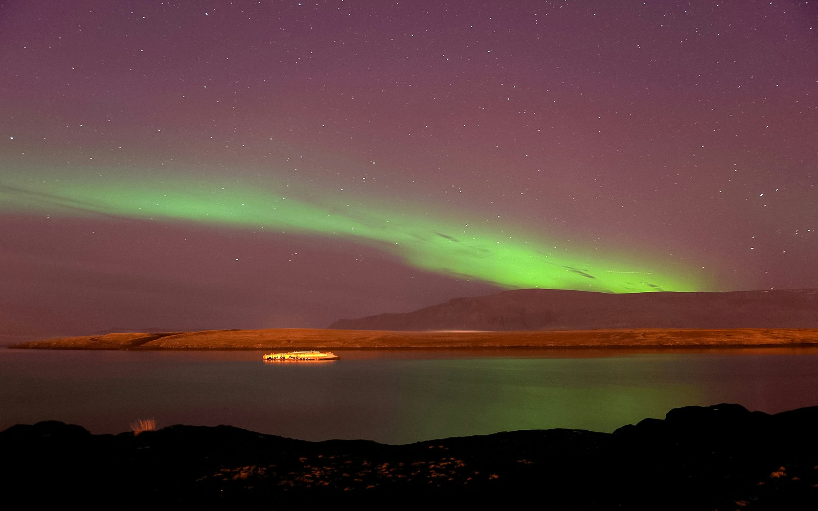Northern Lights over water with a cruise ship near Reykjavik.