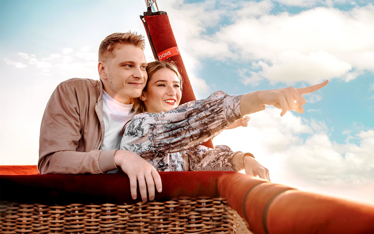 Couple enjoying a hot air balloon ride, pointing at the scenic view.