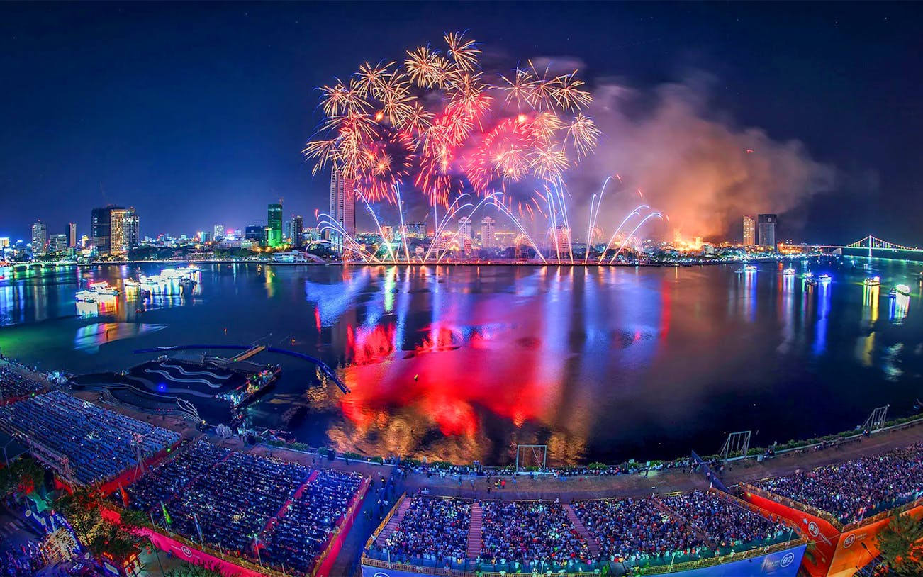 Fireworks over Da Nang skyline during International Fireworks Festival, reflecting on the river.