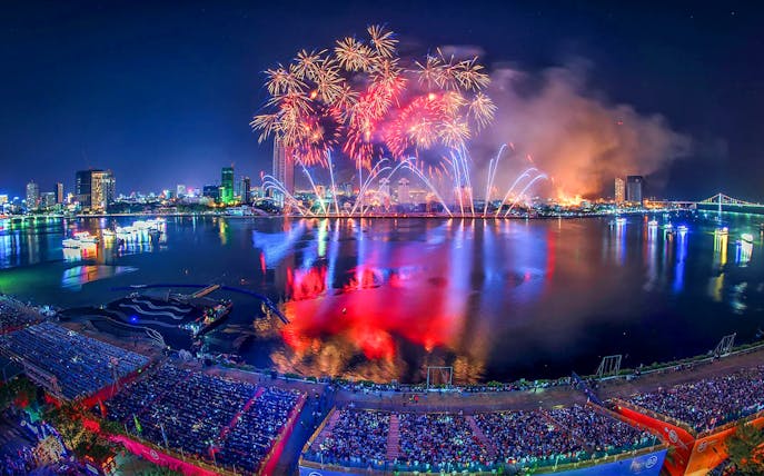 Fireworks over Da Nang skyline during International Fireworks Festival, reflecting on the river.