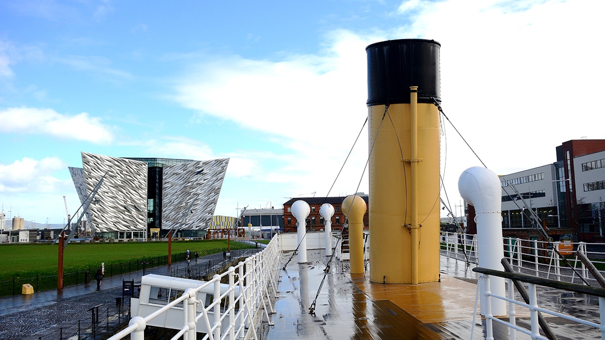 SS Nomadic docked in Belfast with hop-on hop-off tour bus nearby.