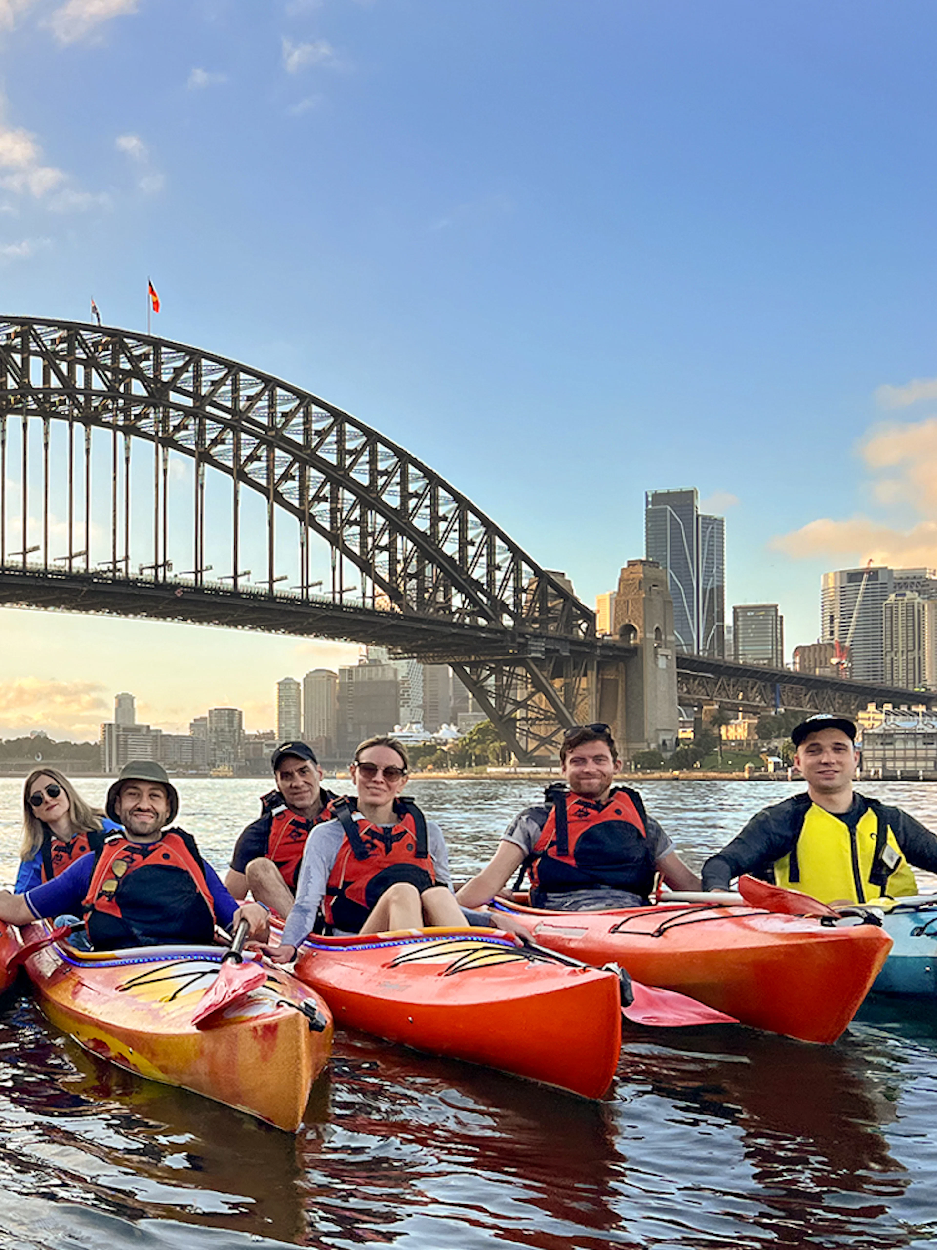 Group kayaking at sunrise on Sydney Harbour with Harbour Bridge and Opera House in view.