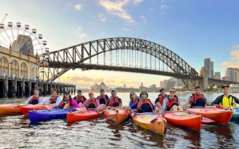 Group kayaking at sunrise on Sydney Harbour with Harbour Bridge and Opera House in view.