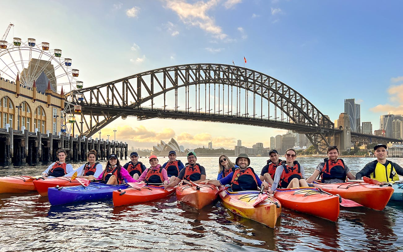 Group kayaking at sunrise on Sydney Harbour with Harbour Bridge and Opera House in view.
