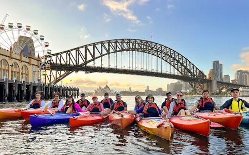 Group kayaking at sunrise on Sydney Harbour with Harbour Bridge and Opera House in view.