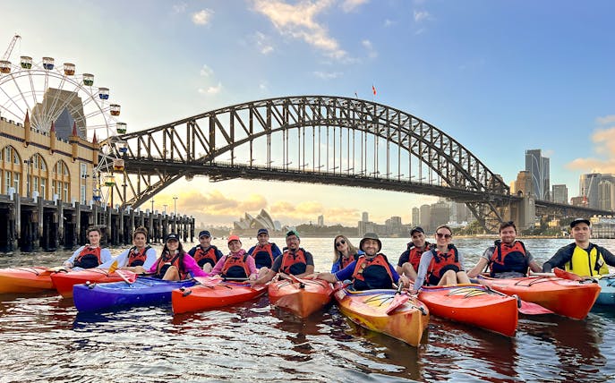 Group kayaking at sunrise on Sydney Harbour with Harbour Bridge and Opera House in view.