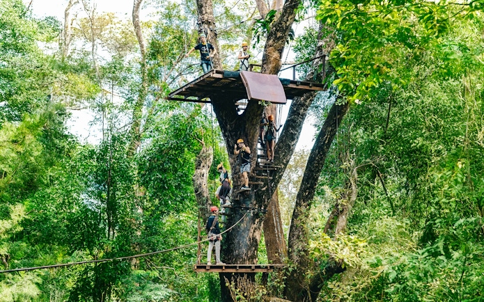 Participants on a zipline platform in a lush forest at Flying Hanuman, Phuket.