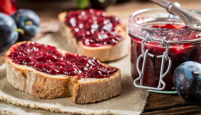 Jam spread on bread kept beside a jar of jam