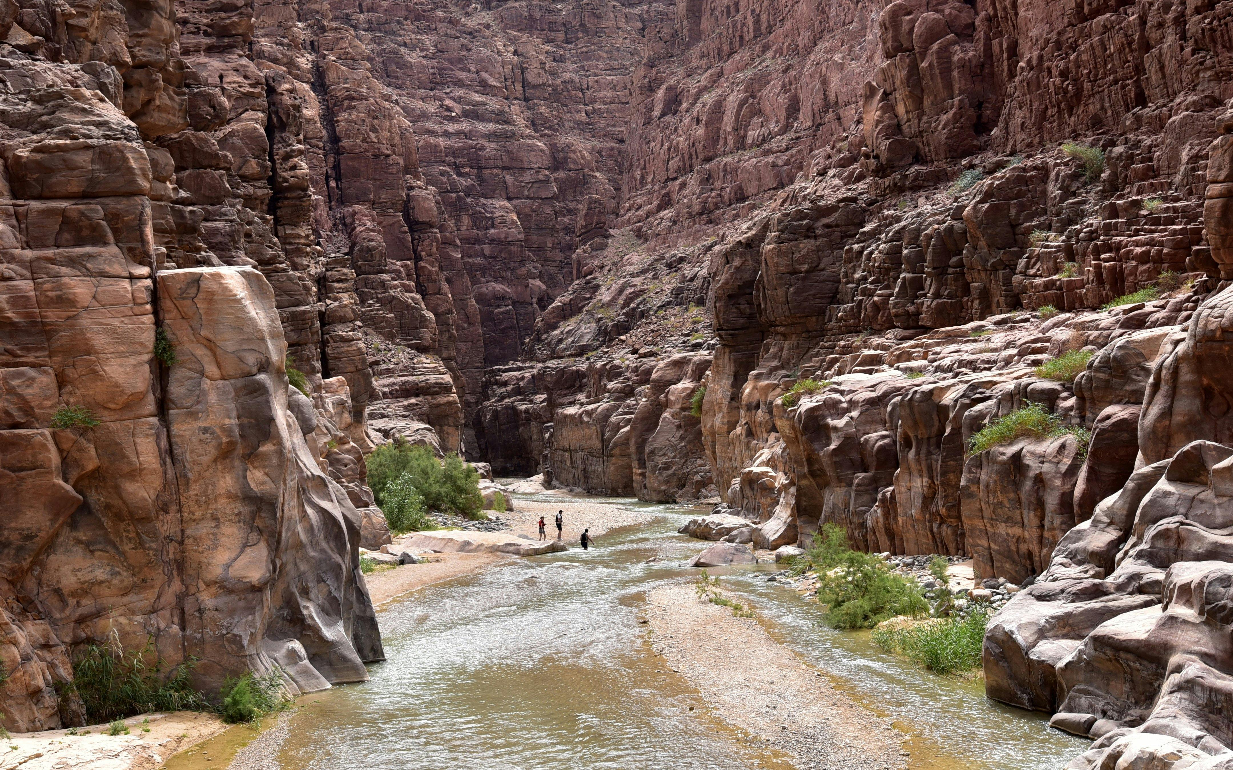 Hikers walking through the canyon of Wadi Mujib, Jordan, with towering rock formations.