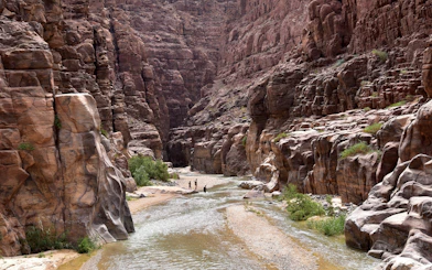 Hikers walking through the canyon of Wadi Mujib, Jordan, with towering rock formations.