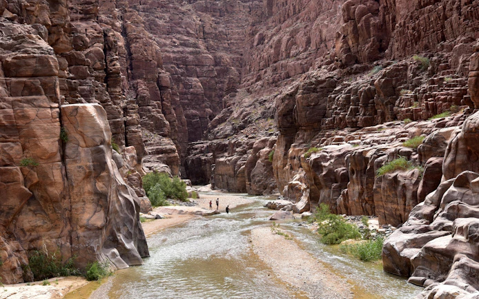 Hikers walking through the canyon of Wadi Mujib, Jordan, with towering rock formations.