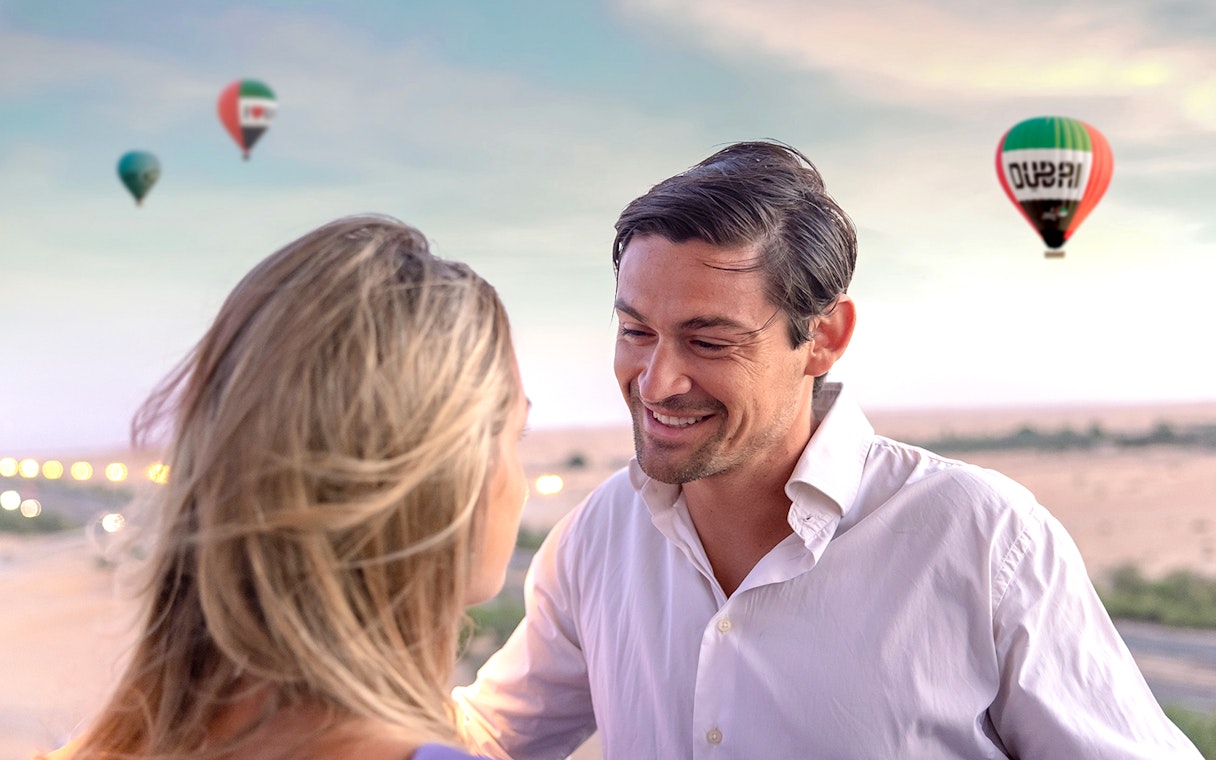 Couple enjoying hot air balloon ride in Dubai desert with balloons in the sky.