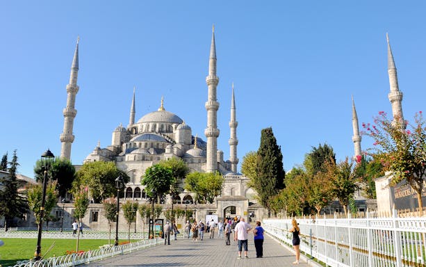 Blue Mosque in Istanbul with tourists walking nearby on a sunny day.