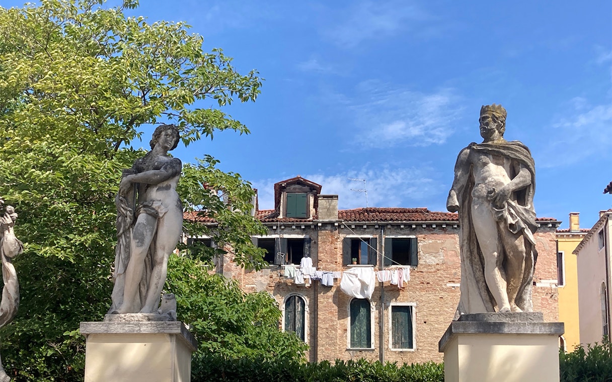 Statues in Ca' Rezzonico Gardens with historic building, Venice.