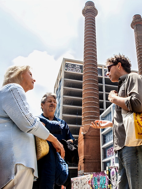 Tour guide discussing Barcelona's Raval history with visitors near graffiti-covered walls and industrial chimneys.