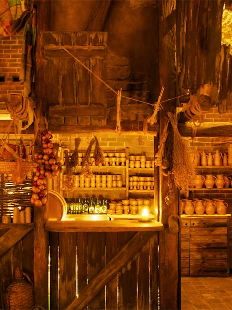 Tavern interior with rustic wooden shelves, clay pots, and hanging herbs for a Medieval Dinner Show.