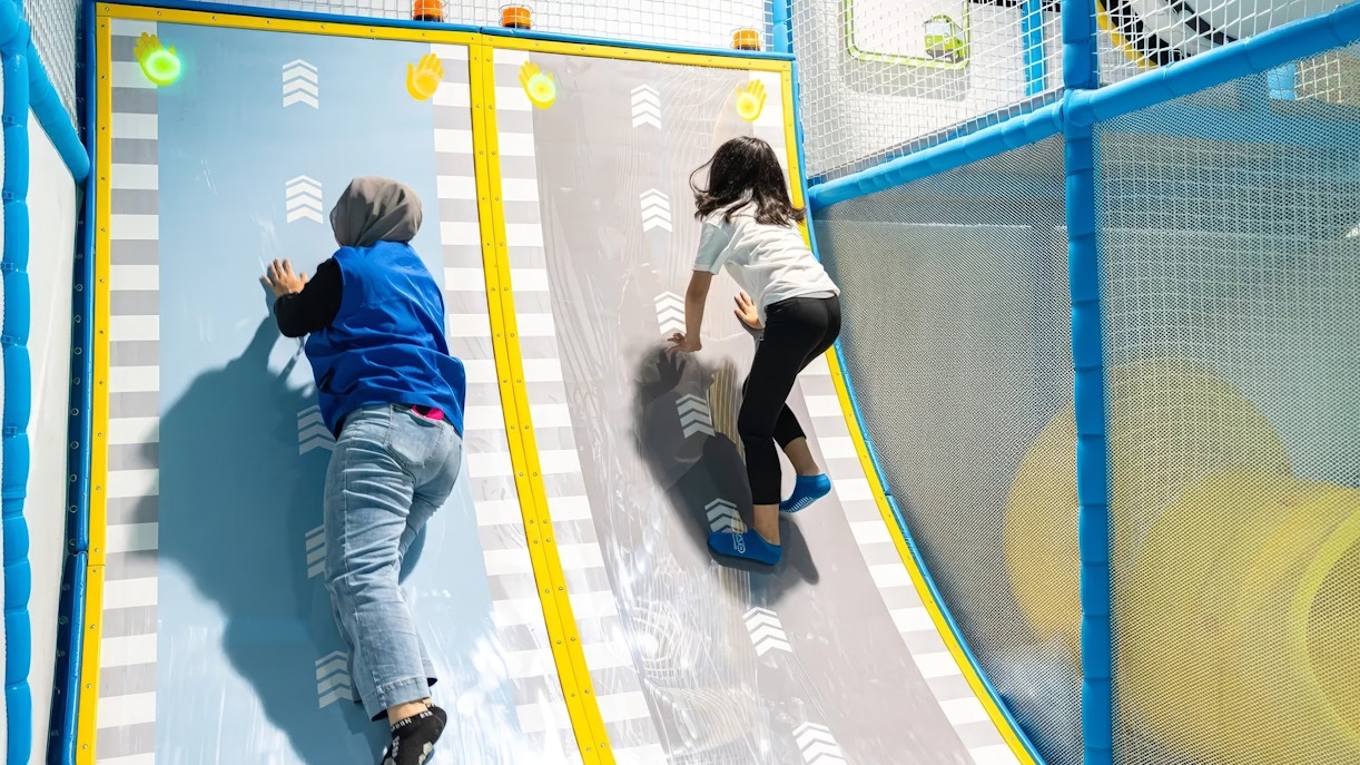 Tourists climbing interactive wall at Tayo Station indoor playground.