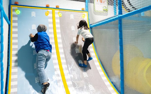 Tourists climbing interactive wall at Tayo Station indoor playground.