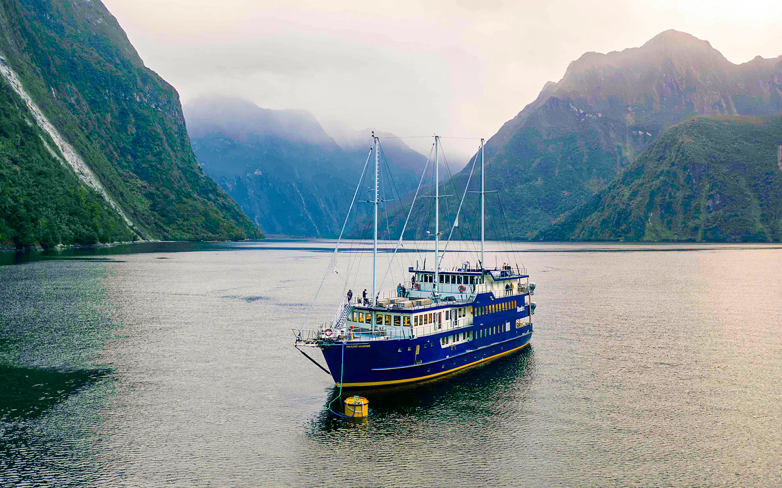 Cruise ship anchored in Milford Sound with misty mountains in the background.