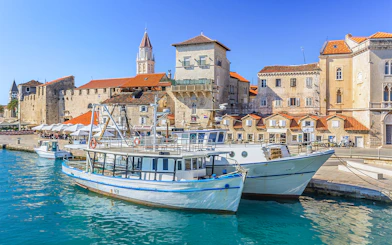 Boats docked in Trogir harbor with historic stone buildings in the background.