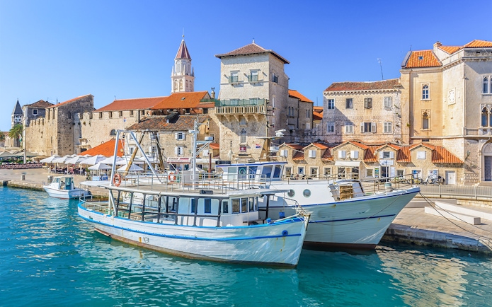 Boats docked in Trogir harbor with historic stone buildings in the background.