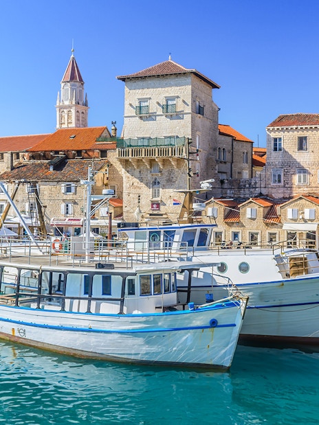 Boats docked in Trogir harbor with historic stone buildings in the background.