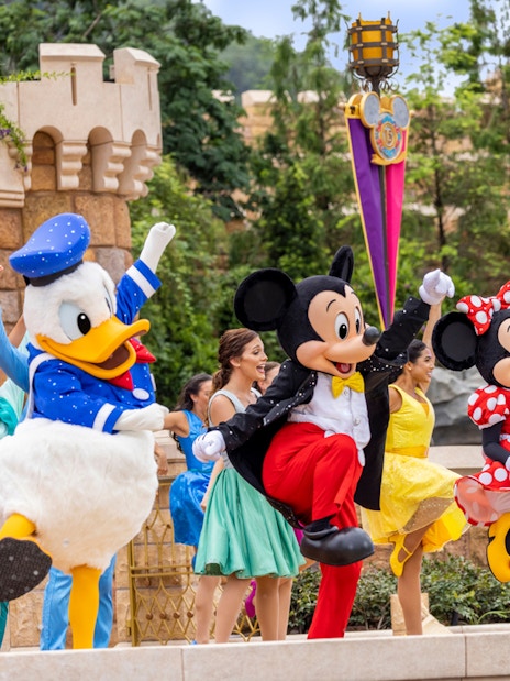 Disney characters performing at Disneyland Hong Kong with castle backdrop.