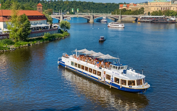 Vltava River cruise boat near Prague's historic bridges and riverside buildings.