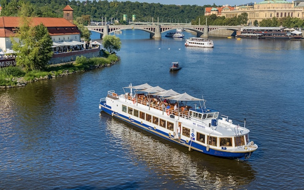 Vltava River cruise boat near Prague's historic bridges and riverside buildings.