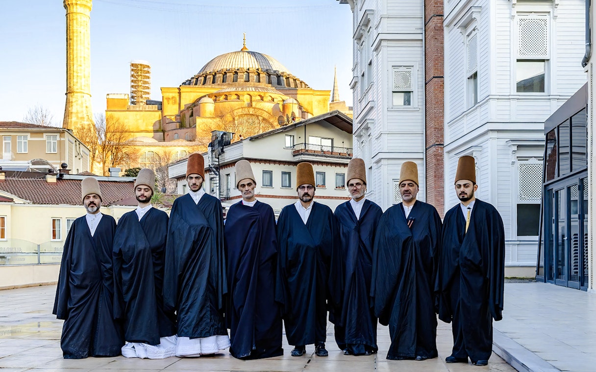 Whirling Dervishes in traditional attire with Hagia Sophia in Istanbul background.